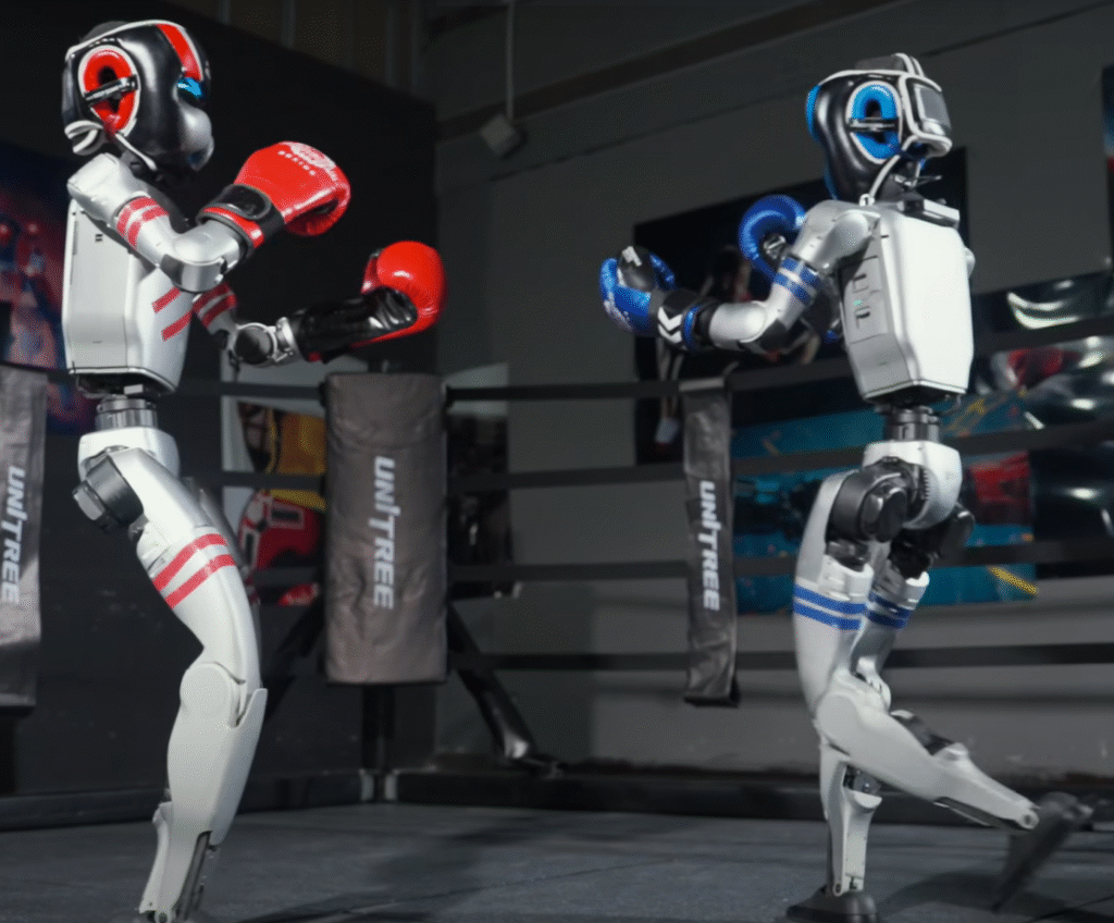 Dois robôs no ringue duelando. à equerda, um robô humanóide com luvas vermelhas e capacete vermelho. A direita, um outro tobô humanoite com luvas e capacete azuis.