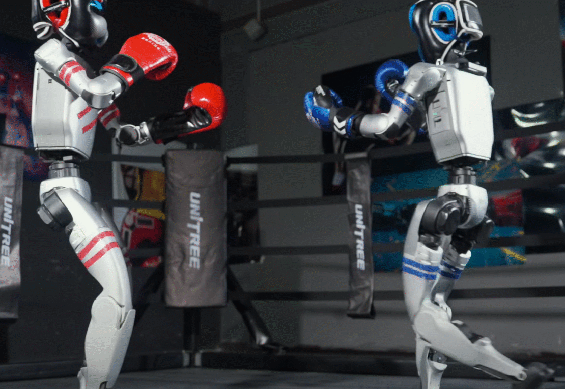 Dois robôs no ringue duelando. à equerda, um robô humanóide com luvas vermelhas e capacete vermelho. A direita, um outro tobô humanoite com luvas e capacete azuis.